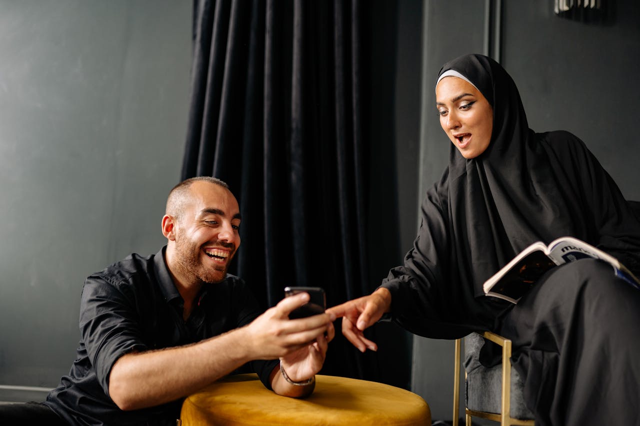 A happy couple in traditional attire laughing and using a smartphone indoors.